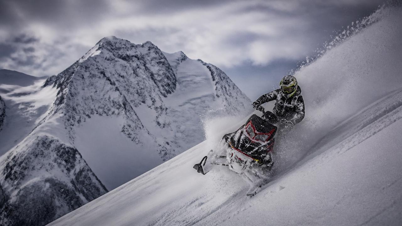 Snowmobile carving deep powder under BC peaks